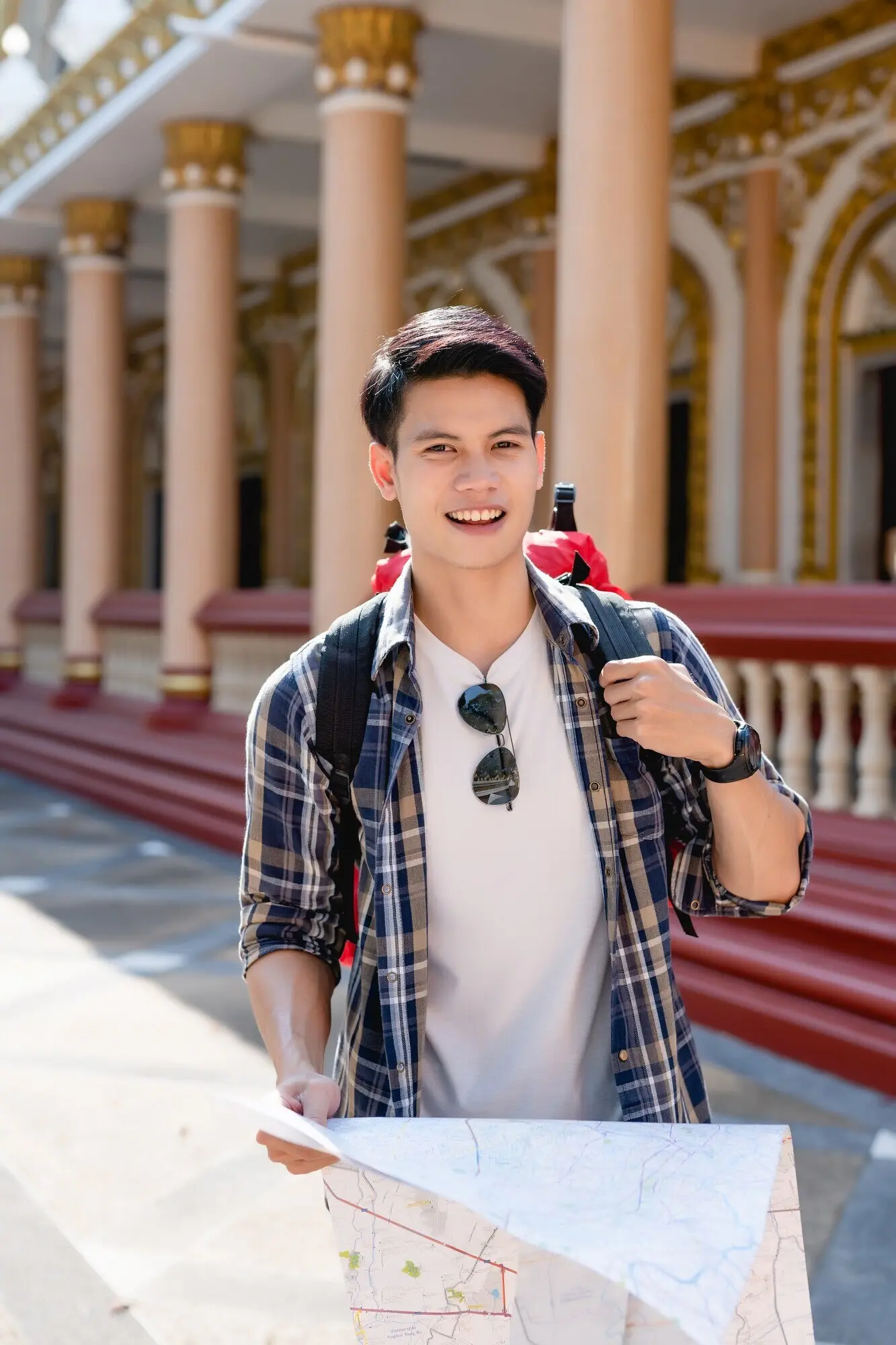 美しいタイの寺院で紙の地図を手に持つ笑顔のアジア人男性バックパッカーのポートレート